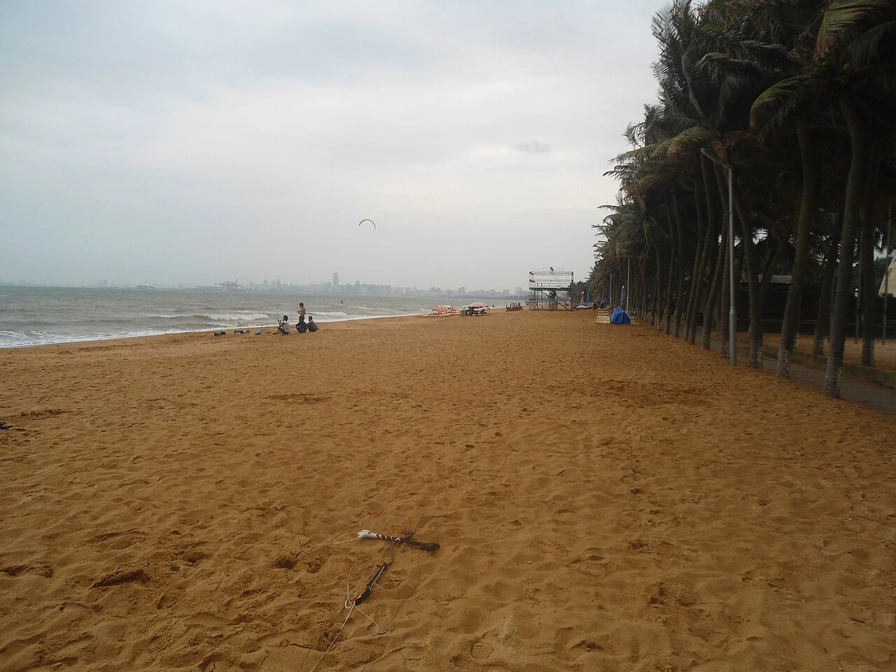 Holiday Beach on the main island of Hainan, Haikou, China, looking east along the beach and coconut palms under an overcast sky.